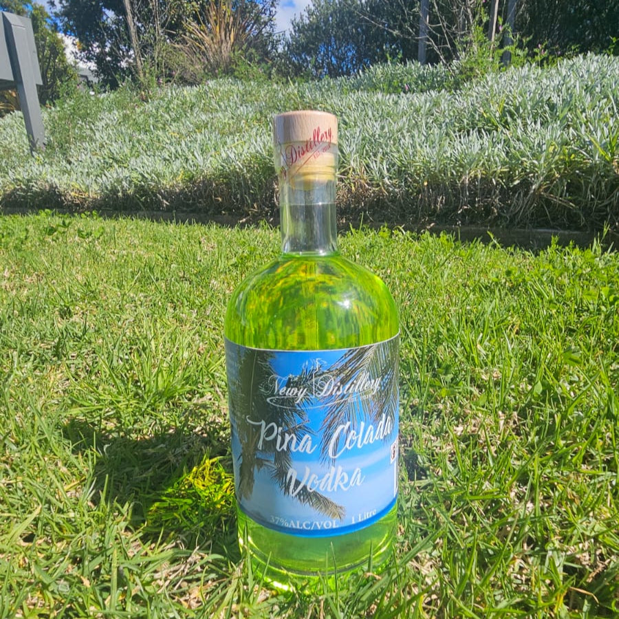 Bottle of Pina Colada Vodka on grass with trees in the background