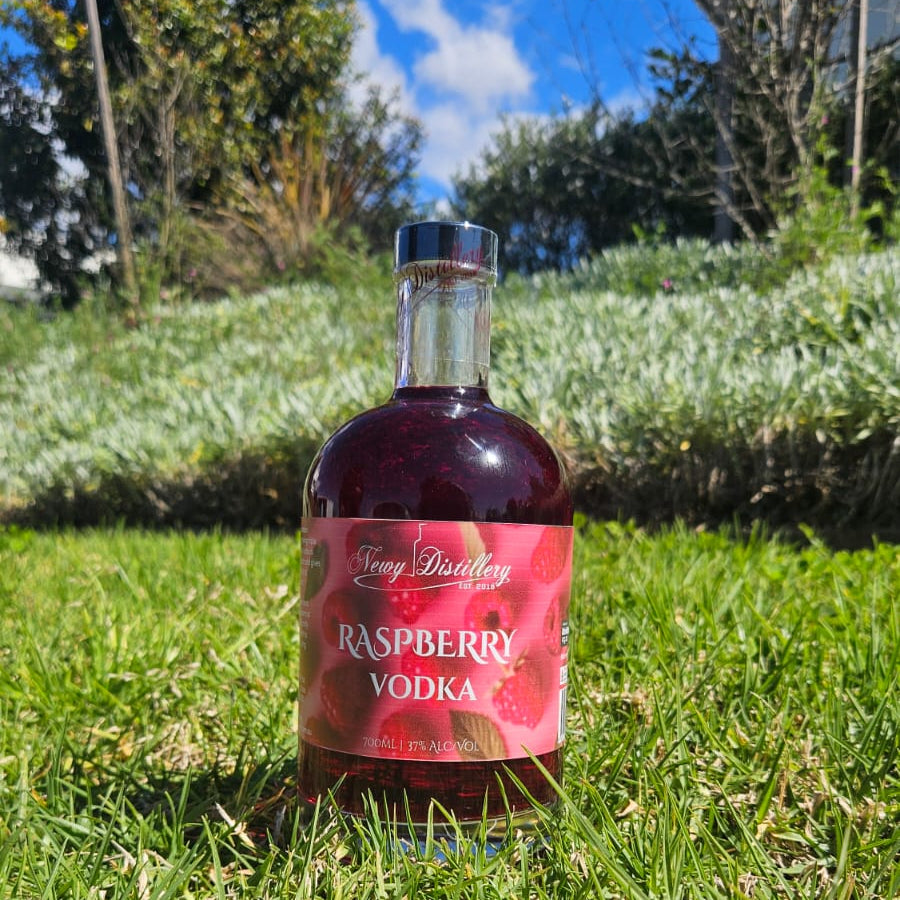 Bottle of Raspberry Vodka on grass with trees in the background