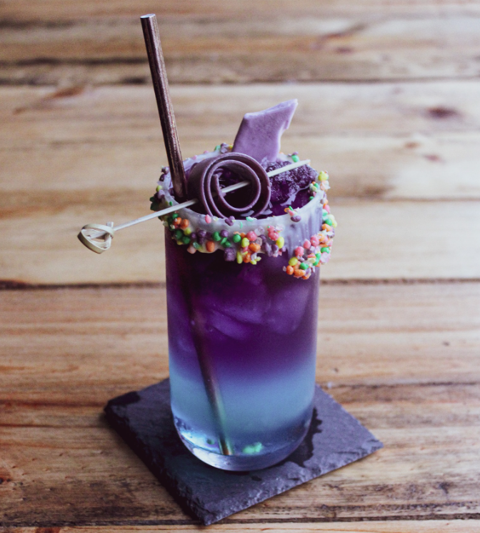 Purple cocktail with a straw and decorative elements on a wooden surface
