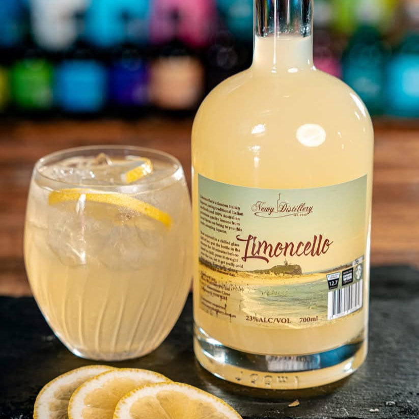 Bottle of limoncello with a glass of lemonade and lemon slices on a bar counter.