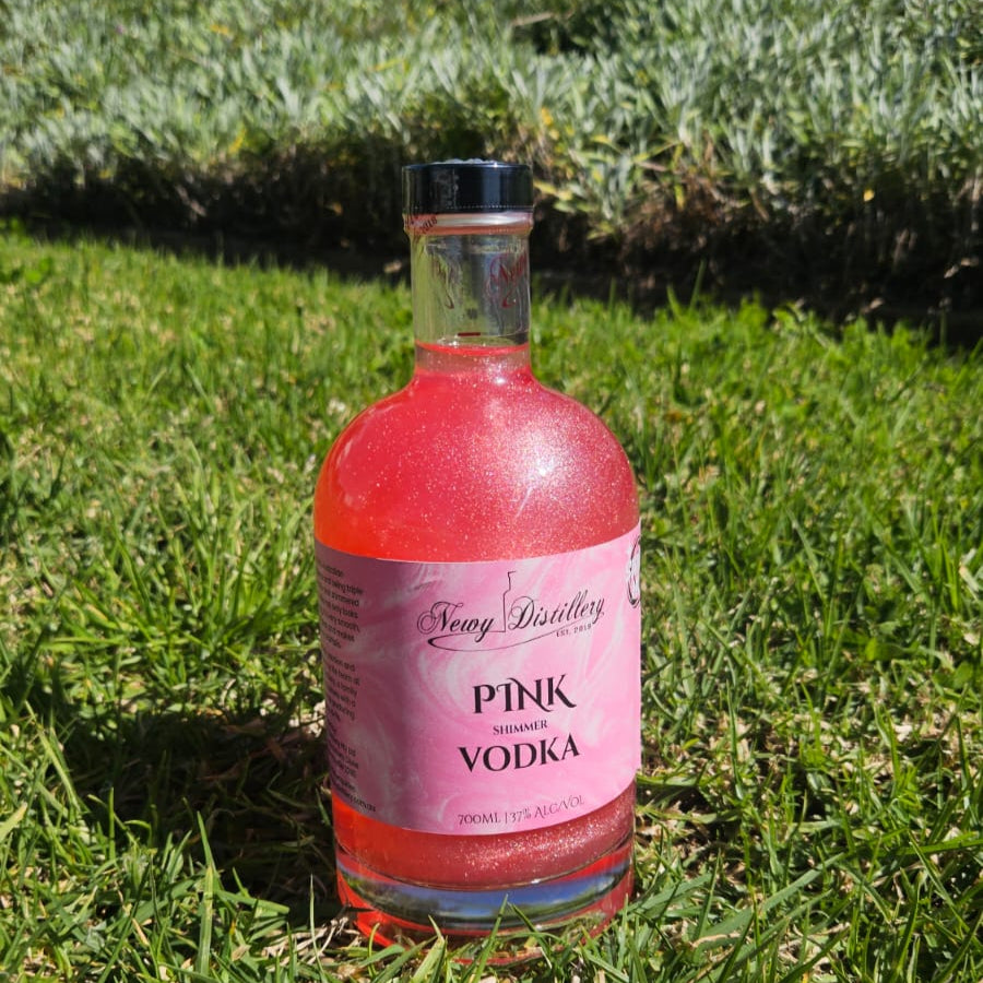 Bottle of pink vodka on grass with plants in the background