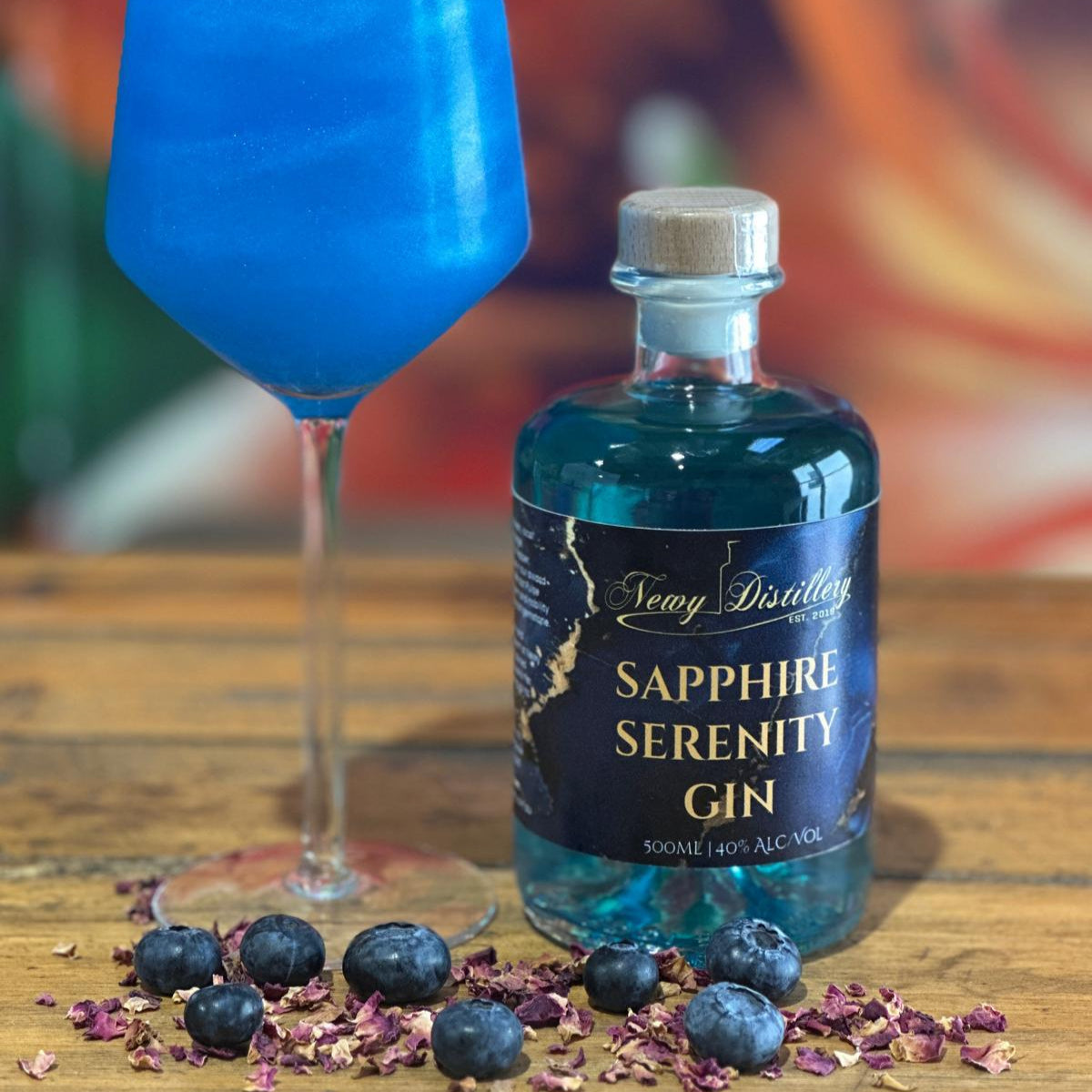 Bottle of Sapphire Serenity Gin with a blue cocktail in a glass on a wooden surface.