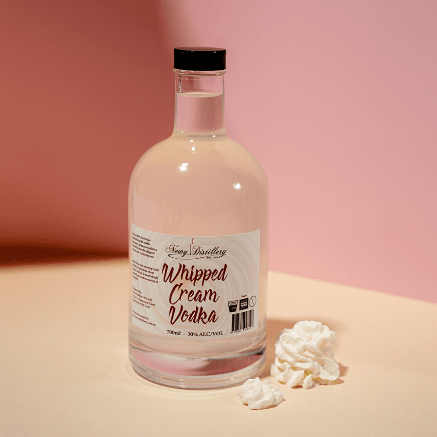 Whipped Cream Flavoured Vodka by Newy Distillery. 700ml 30% alcoho/volume. Delicious Whipped Cream flavour triple distilled vodka displayed upright with whipped cream buds against pink background.