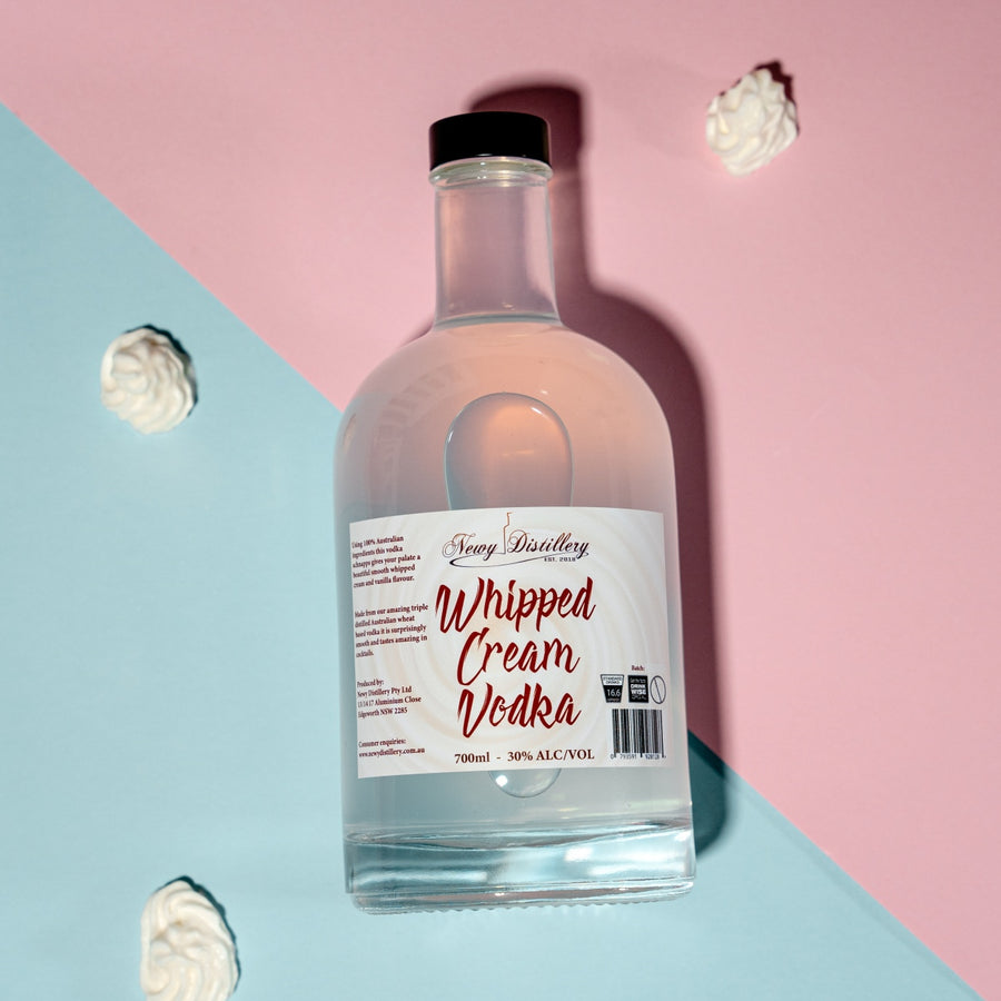 Whipped Cream Flavoured Vodka by Newy Distillery. 700ml 30% alcoho/volume. Delicious Whipped Cream flavour triple distilled vodka displayed with bottle laid down whipped cream buds against pink and blue background.