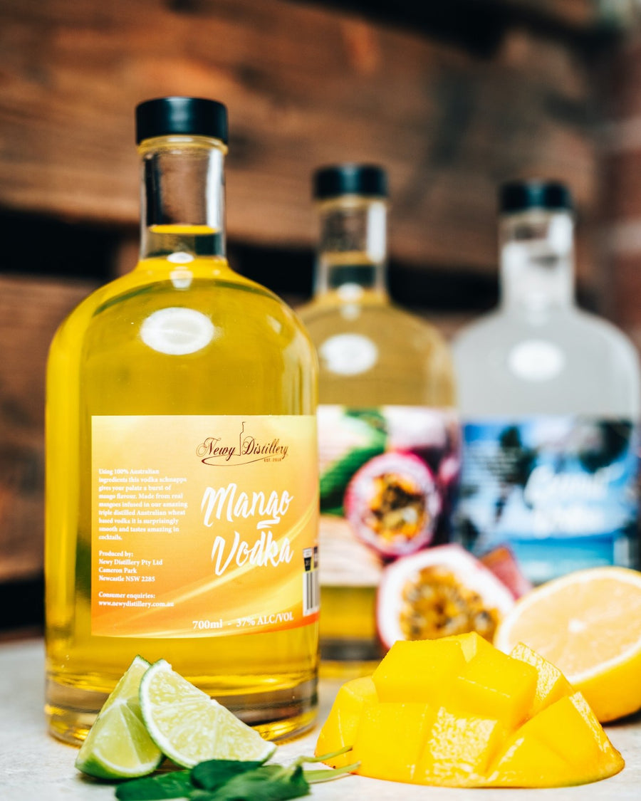 Mango Fruit Infused Vodka by Newy Distillery. 700ml bottle displayed on wooden deck with fresh mango and limes.