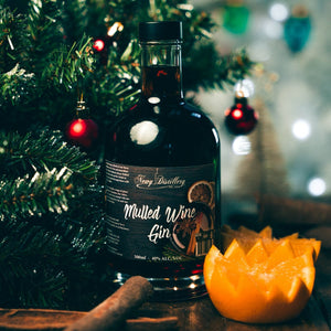 Mulled Wine Gin by Newy Distillery. Award Winning Gin. 500ml bottle displayed in christmas scene with green Christmas Tree and fresh orange.