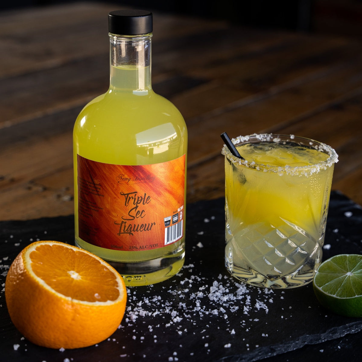 Triple Sec Gin Liqueur 500ml displayed on grey slate next to mango cocktail with fresh orange garnish. Triple Sec Gin Liqueur, fruit gin liqueur by Newy Distillery.
