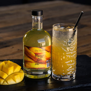 Mango Gin Liqueur 700ml bottle displayed next mango cocktail in tall glass with fresh mango garnish. Mango gin lIqueur, fruit gin liqueur by Newy Disitllery.
