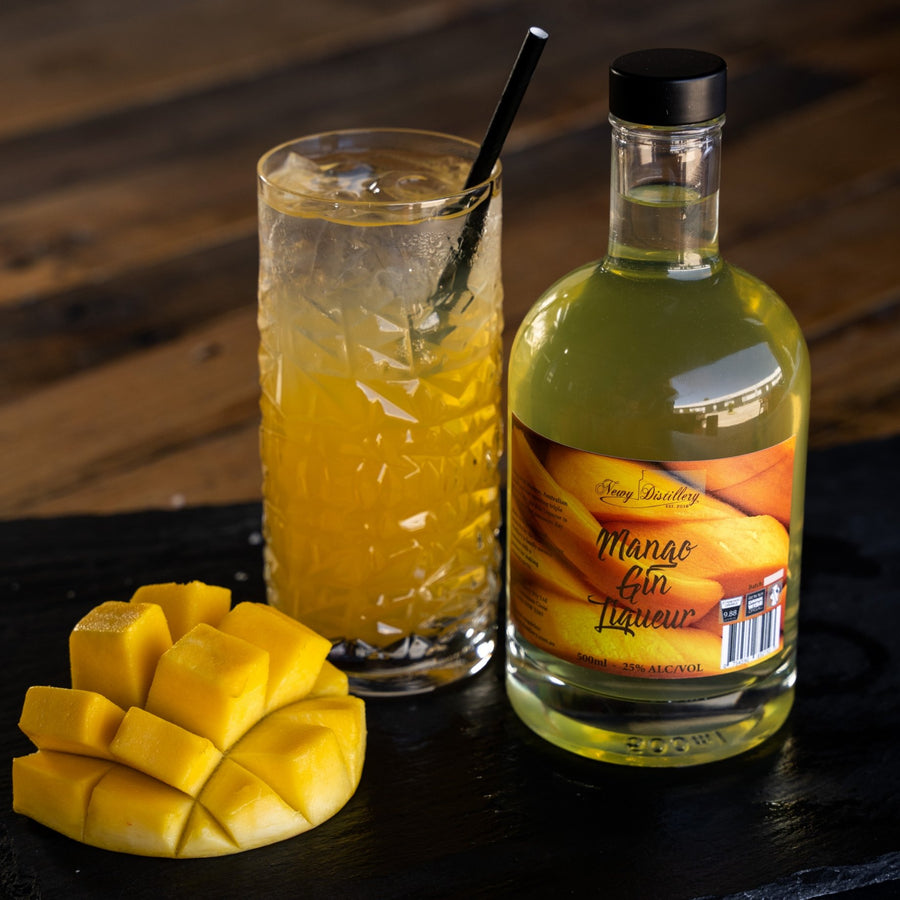 Mango Gin Liqueur 500ml displayed on grey slate next to mango cocktail with fresh mango garnish. Mango Gin Liqueur, fruit gin liqueur by Newy Distillery.