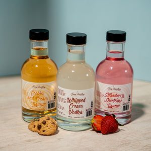 Newy Distillery Vodka Dessert Range mini pack with blue background and mini cookies and fresh strawberry.Contains: 1x200ml whipped cream vodka, 1x 200ml cookies and cream vodka liqueur, 1x200ml strawberry shortcake vodka liqueur. Flavoured vodka. Cake flavoured vodka.