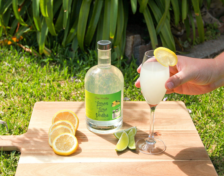 Lemon Lime Fruit Infused Vodka by Newy Distillery. 700ml bottle displayed on wooden board in garden with cocktail and lemon and lime garnish.